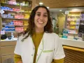 Une souriante préparatrice en pharmacie en Espagne, entourée de boîtes de médicaments sur les étagères.