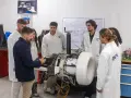 Des étudiants en blouse blanche observent un moteur complexe dans un laboratoire d'école d'ingénieur en Belgique.