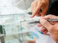 Un homme en costume regarde des graphiques financiers. Des mains analysent des données, suggérant une licence finance à distance.