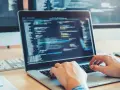 Des mains tapant sur un clavier d'ordinateur portable affichant du code. Une opportunité de formation informatique sans bac pour un avenir prometteur.