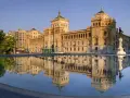 Le majestueux bâtiment du **universidad de valladolid** se reflète dans l'eau calme d'une fontaine, sous un ciel bleu clair.