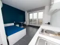 Chambre moderne pour étudiant à Luxembourg : lit bleu, bureau, kitchenette et balcon avec vue.