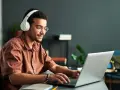 Jeune homme souriant avec des écouteurs, concentré sur son ordinateur portable. Il suit un master informatique à distance, profitant de la flexibilité de l'apprentissage en ligne.