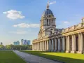 Le bâtiment néoclassique de l'université de Greenwich, avec son dôme et ses colonnes imposantes, se dresse sous un ciel bleu clair.