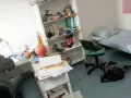 Bureau désordonné, lit simple, étagère remplie d'articles divers. Un ordinateur portable sur une chaise. Une scène typique pour trouver un logement en Belgique.