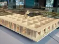 Maquette en bois d'une école d'architecture belge, avec des figures stylisées et des plantes.