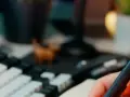 Main tenant une plume, prêt à étudier pour sa licence sociologie à distance. Un clavier mécanique et une petite figurine complètent le décor.