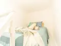 Lit douillet dans un logement étudiant à Budapest, avec des coussins bleus et verts, et des plaids beiges.