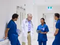 Une équipe médicale discute dans un couloir d'hôpital. Un médecin en blouse blanche échange avec trois infirmiers en uniforme bleu. Ils semblent discuter d'un cas, peut-être en lien avec du infirmier en ligne.