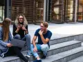 Trois jeunes discutent sur des marches, l'un regarde son téléphone, l'autre un ordinateur portable. Ils semblent parler du cout de la vie aux Pays-Bas.