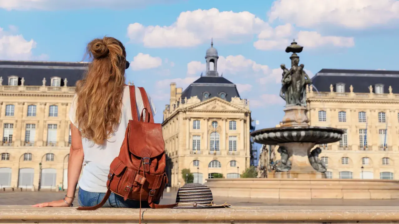 Jeune femme avec un sac à dos en cuir, profitant de sa **année de césure** à Bordeaux, devant la fontaine de la Place de la Bourse.