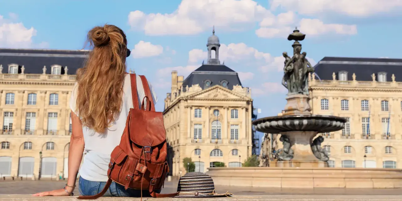 Jeune femme avec un sac à dos en cuir, profitant de sa **année de césure** à Bordeaux, devant la fontaine de la Place de la Bourse.