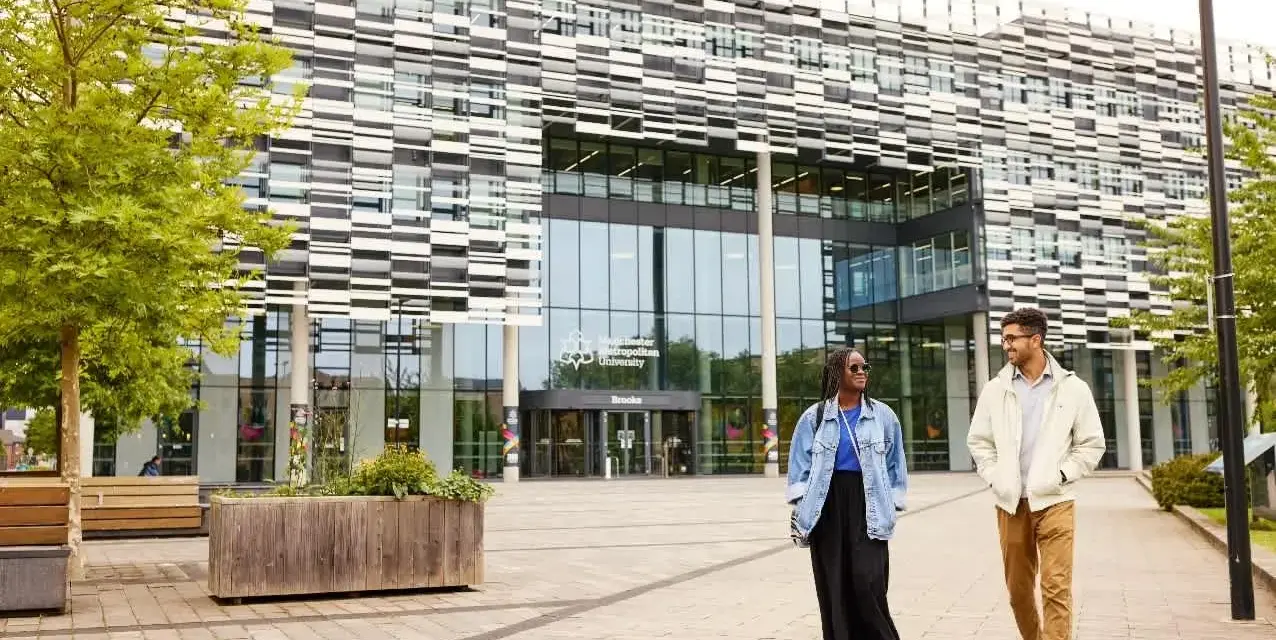 Deux étudiants marchent devant l'université métropolitaine de Manchester, un bâtiment moderne avec une façade à motifs.