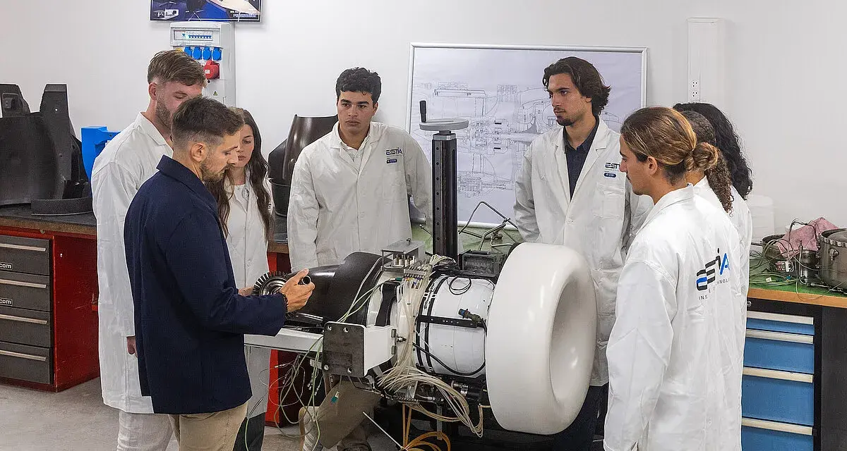 Des étudiants en blouse blanche observent un moteur complexe dans un laboratoire d'école d'ingénieur en Belgique.