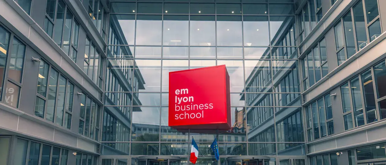 Le logo rouge d'EM Lyon Business School flotte devant un bâtiment moderne en verre. Idéal pour un master project management.