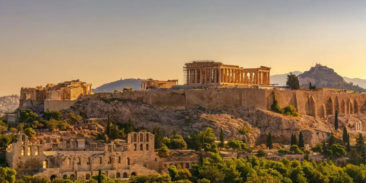 L'Acropole d'Athènes baignée de soleil, un site historique qui rappelle le coût de la vie en Grèce, entre ruines antiques et verdure luxuriante.