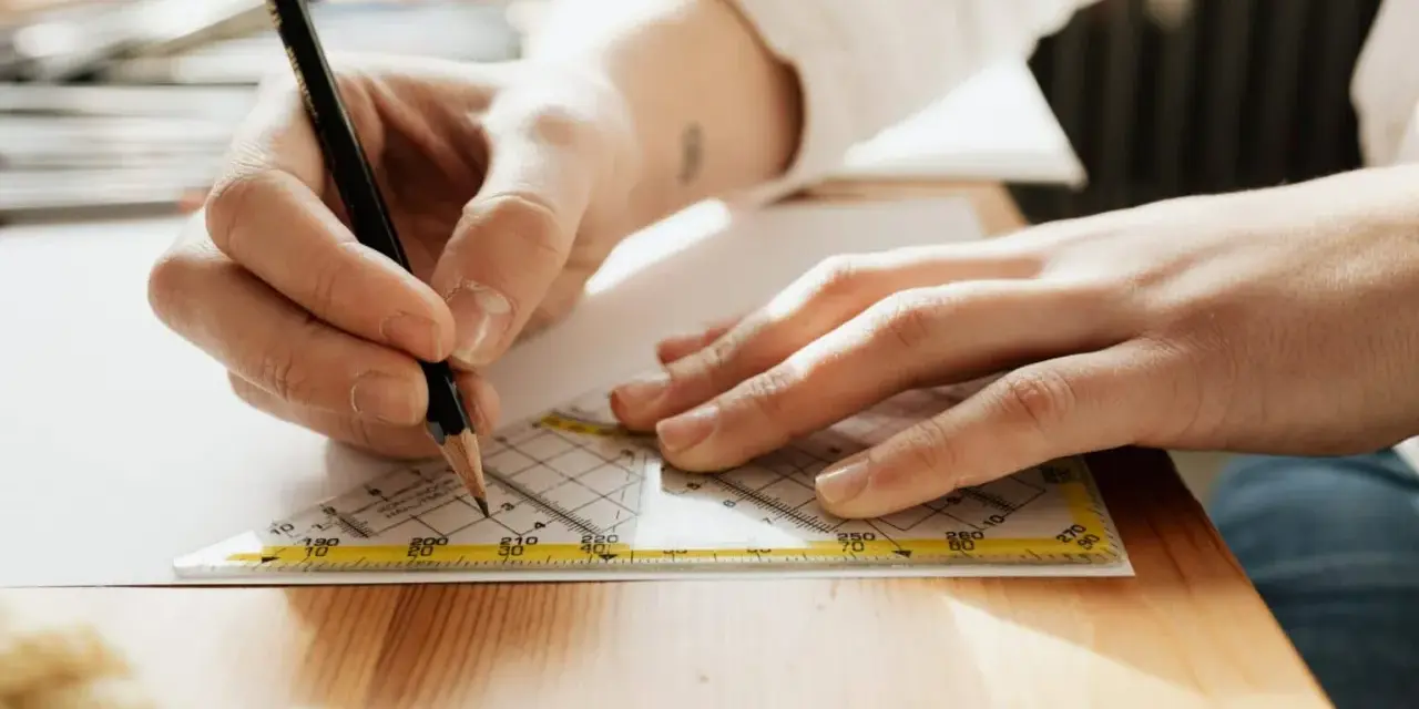 Main d'un étudiant en BTS Design d'Espace à Paris traçant une ligne précise avec un crayon et une équerre sur une feuille.
