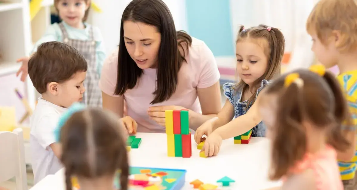 Une enseignante, experte en psychopédagogie à distance, guide des enfants jouant avec des blocs colorés.