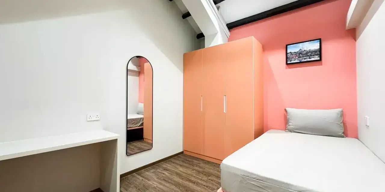 Chambre moderne pour **logement étudiant à Singapour** : lit, bureau, armoire corail et miroir mural.