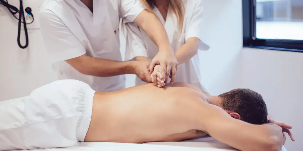 Des étudiants de l'école kine Gérone apprennent la kinésithérapie en pratiquant sur un patient allongé.