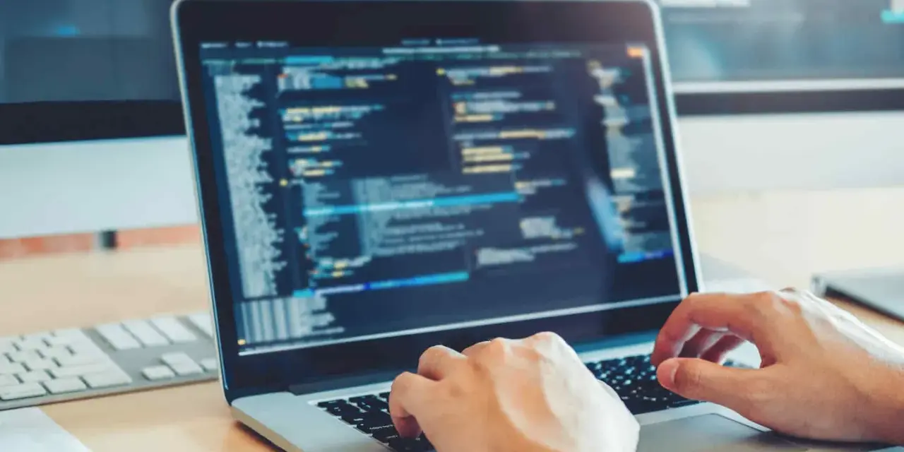 Des mains tapant sur un clavier d'ordinateur portable affichant du code. Une opportunité de formation informatique sans bac pour un avenir prometteur.