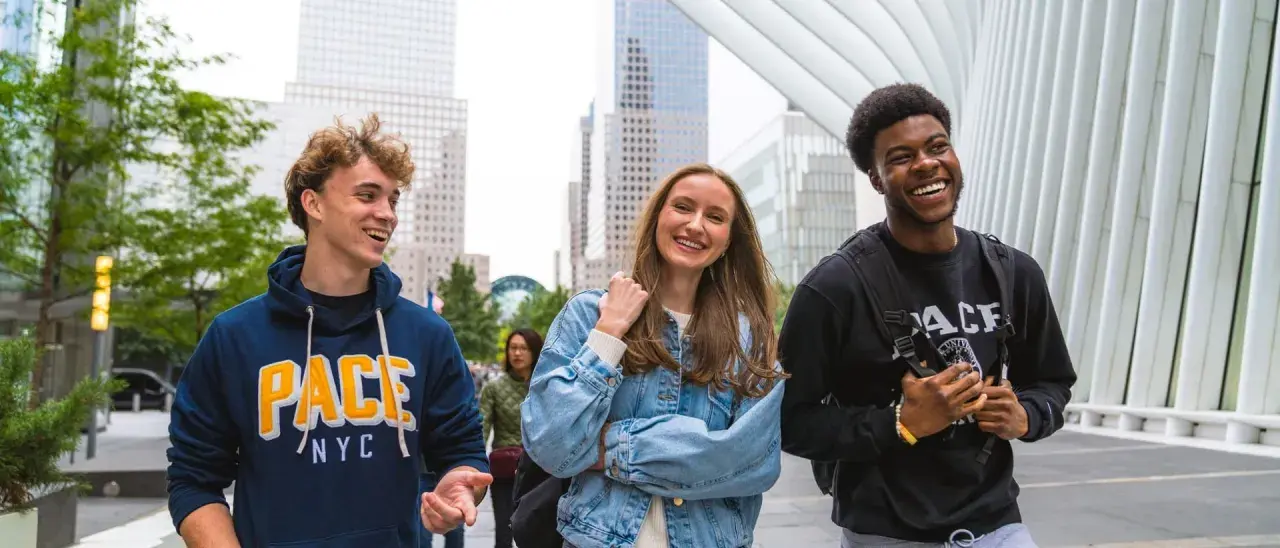 Trois étudiants souriants marchent dans le quartier financier de New York, un lieu idéal pour un MBA.