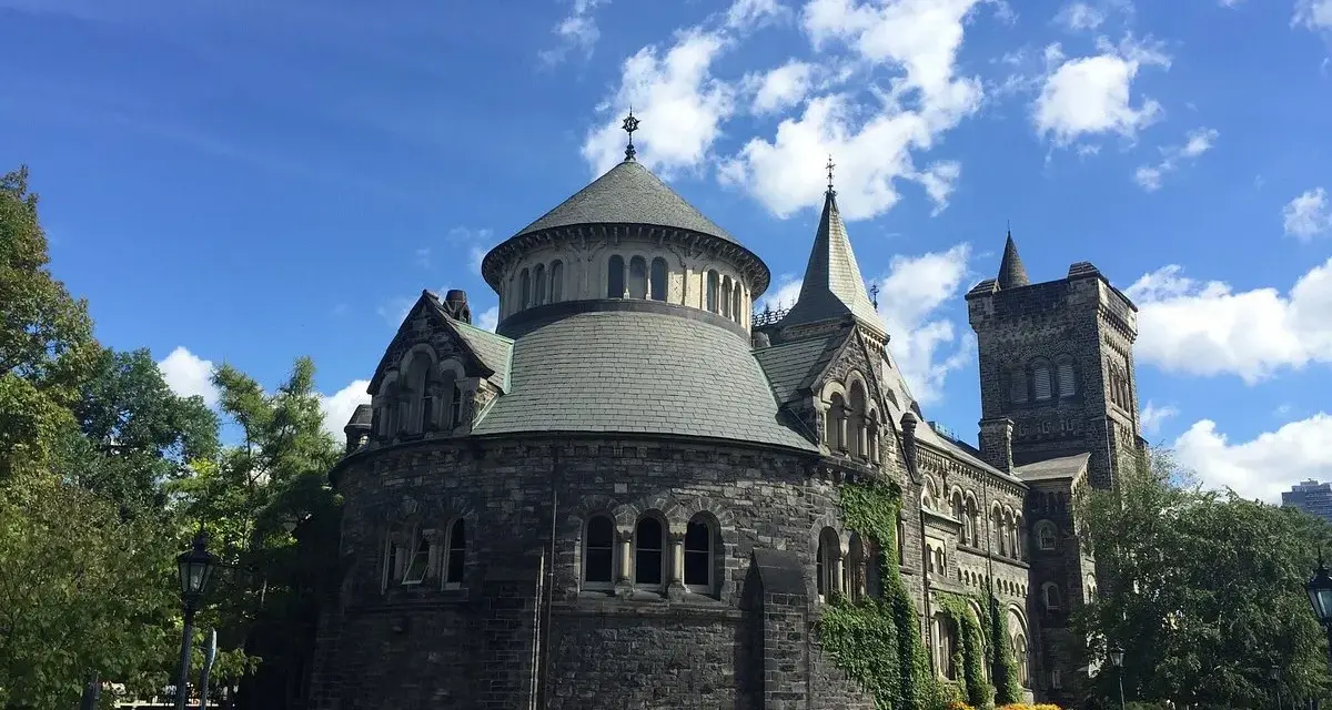 Bâtiment historique en pierre, rappelant une école de cinéma à Toronto, sous un ciel bleu et nuageux.