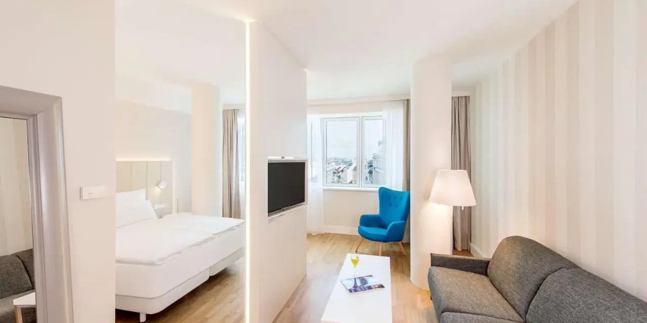 Chambre moderne avec lit, canapé, TV et vue sur la ville. Idéal pour un logement étudiant à Vienne, Autriche.