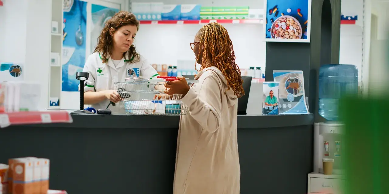 Une pharmacienne conseille une cliente. Une affiche sur la formation préparateur en pharmacie à distance est visible.