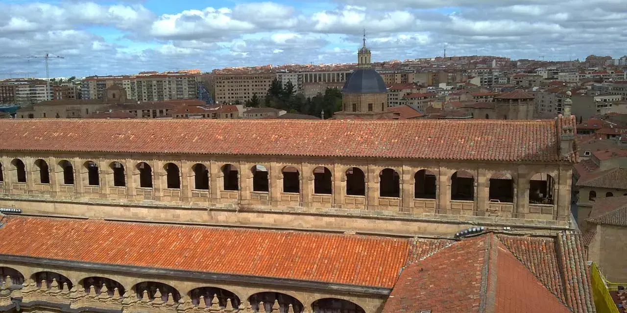 Vue aérienne de l'université pontificale de Salamanque, avec ses toits de tuiles rouges et son dôme emblématique sous un ciel nuageux.