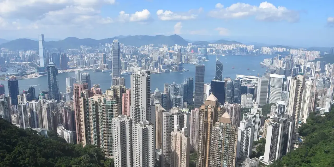 Vue panoramique de Hong Kong, avec ses gratte-ciel s'étendant jusqu'à l'horizon. On aperçoit le campus de la Hong Kong Baptist University, niché au milieu de la verdure luxuriante.