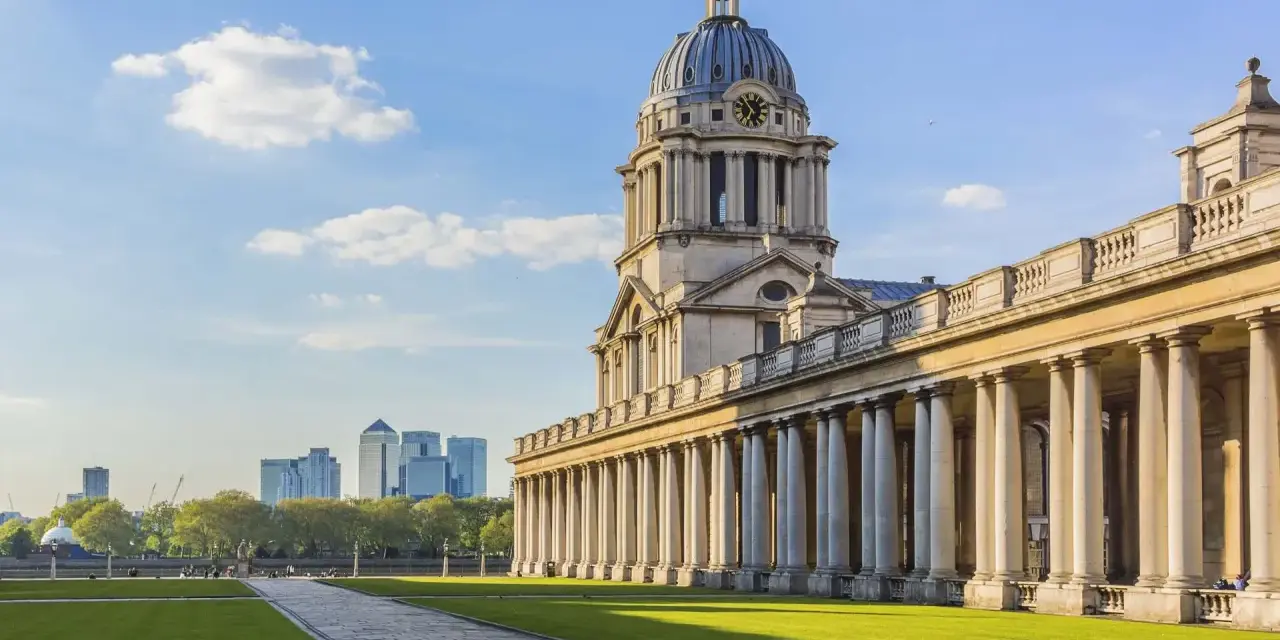 Le bâtiment néoclassique de l'université de Greenwich, avec son dôme et ses colonnes imposantes, se dresse sous un ciel bleu clair.