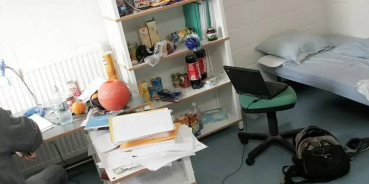 Bureau désordonné, lit simple, étagère remplie d'articles divers. Un ordinateur portable sur une chaise. Une scène typique pour trouver un logement en Belgique.