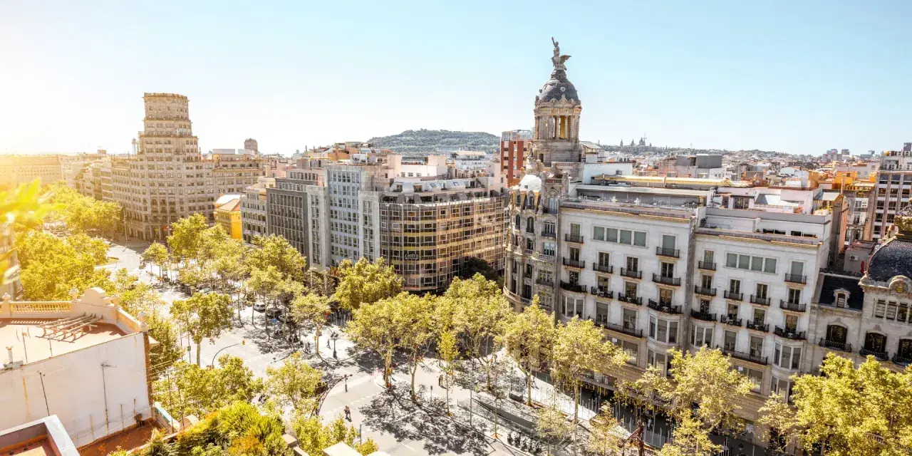 Vue aérienne de Barcelone, ville dynamique qui pourrait figurer dans le classement université espagne. Bâtiments haussmanniens, arbres luxuriants et ciel bleu.