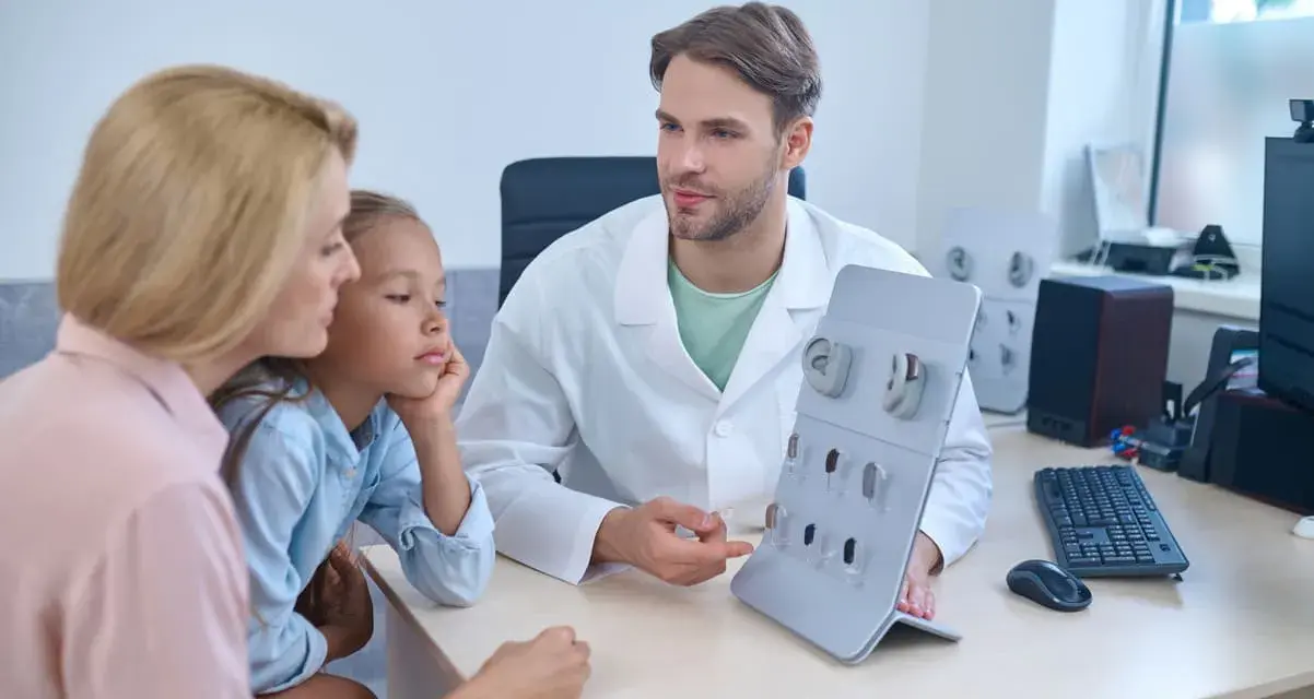 Un audioprothésiste explique des appareils auditifs à une mère et sa fille. Une scène qui pourrait illustrer la formation accélérée audioprothésiste.