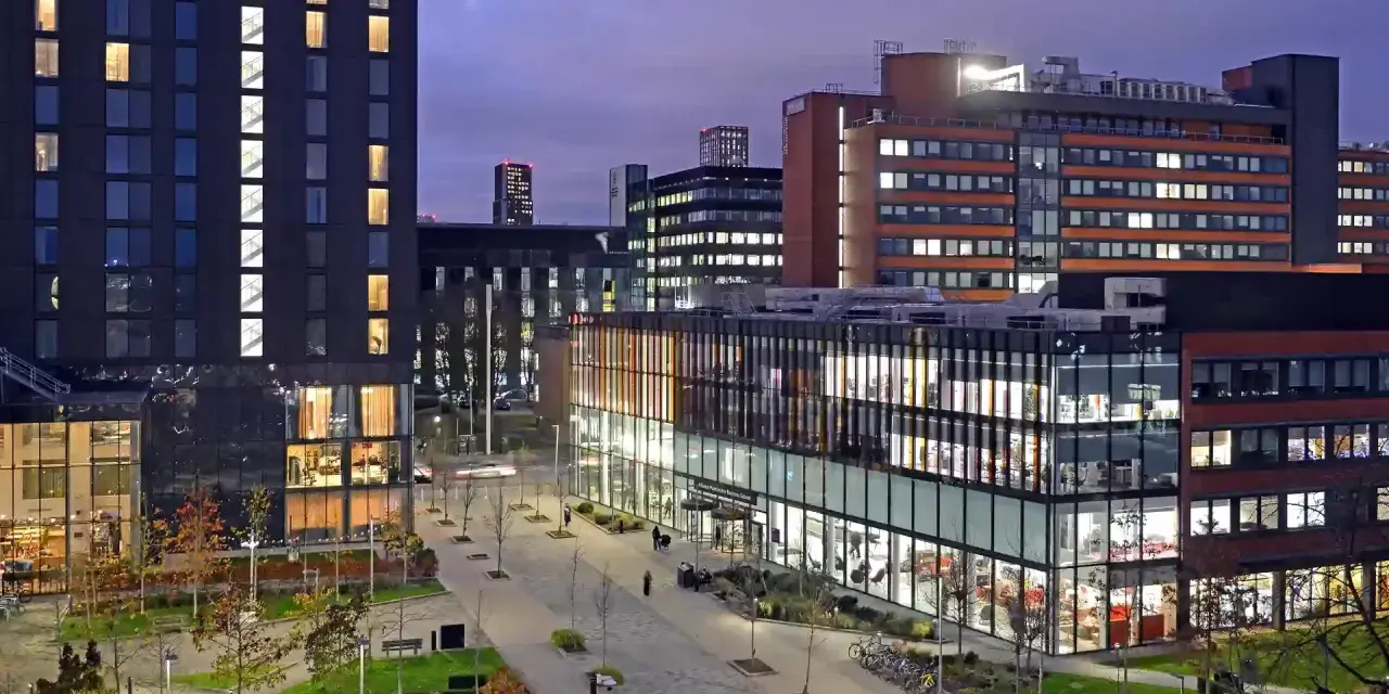 Bâtiments modernes illuminés le soir, avec une enseigne Alliance Manchester Business School visible.