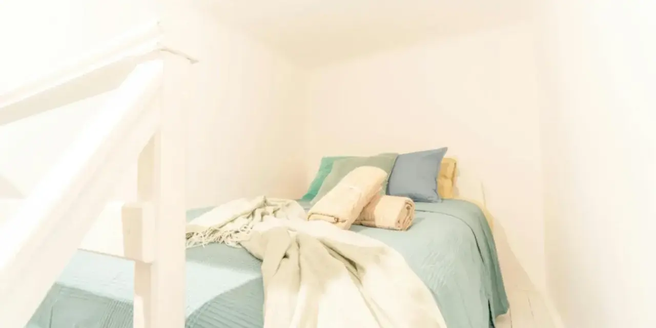Lit douillet dans un logement étudiant à Budapest, avec des coussins bleus et verts, et des plaids beiges.