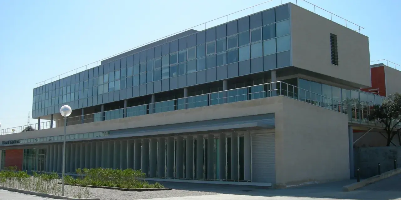 Bâtiment moderne aux lignes épurées, possiblement une école d'élite à Madrid, avec de grandes baies vitrées et une façade en pierre claire.