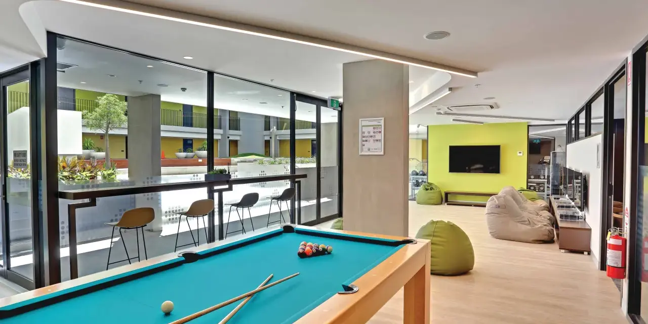 Salle commune moderne pour logement étudiant à Sydney, avec table de billard, poufs et espace extérieur visible.