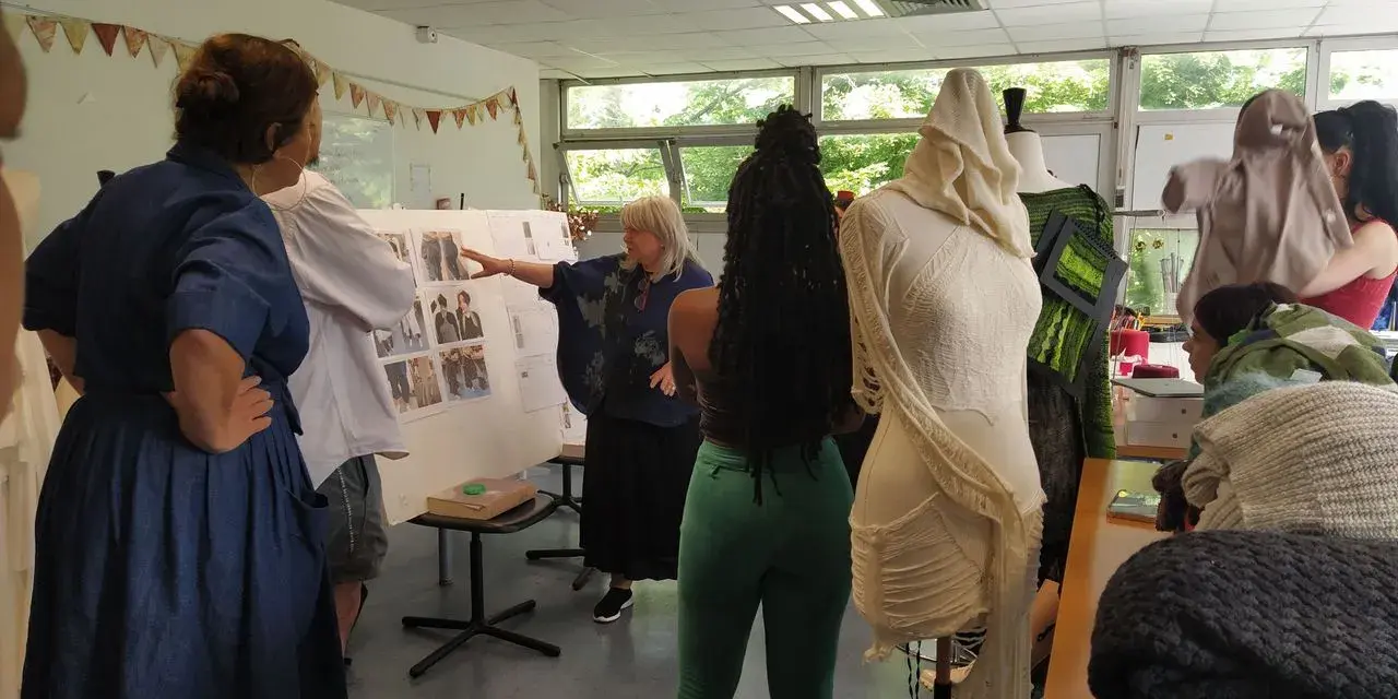 Des élèves d'une école de mode gratuite présentent leurs créations sur des mannequins. Une enseignante explique un tableau d'inspiration.
