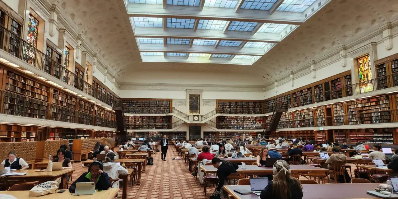 Vaste bibliothèque avec étudiants travaillant sur leurs ordinateurs portables, un décor idéal pour une licence science politique à distance.