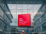 Le logo rouge d'EM Lyon Business School flotte devant un bâtiment moderne en verre. Idéal pour un master project management.