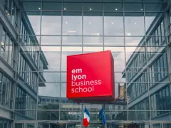 Le logo rouge d'EM Lyon Business School flotte devant un bâtiment moderne en verre. Idéal pour un master project management.