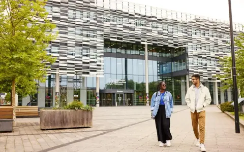 Deux étudiants marchent devant l'université métropolitaine de Manchester, un bâtiment moderne avec une façade à motifs.
