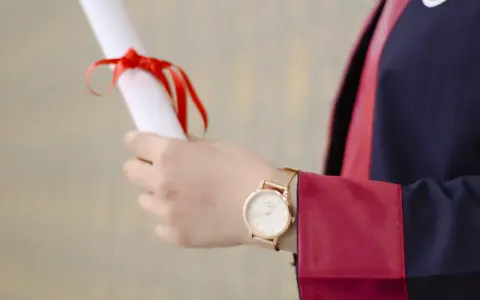 Main tenant un diplôme, une personne porte une robe de doctorat en anglais.