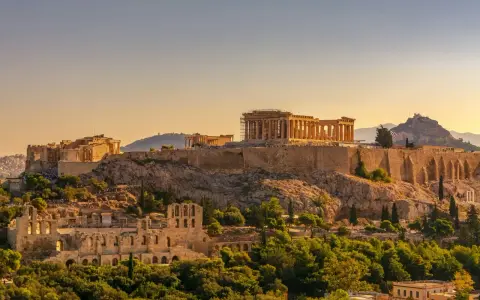 L'Acropole d'Athènes baignée de soleil, un site historique qui rappelle le coût de la vie en Grèce, entre ruines antiques et verdure luxuriante.