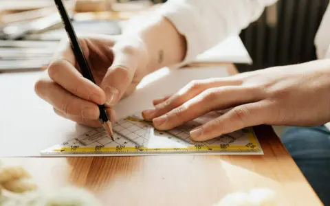 Main d'un étudiant en BTS Design d'Espace à Paris traçant une ligne précise avec un crayon et une équerre sur une feuille.