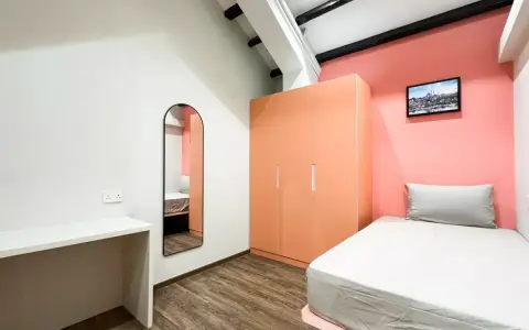 Chambre moderne pour **logement étudiant à Singapour** : lit, bureau, armoire corail et miroir mural.