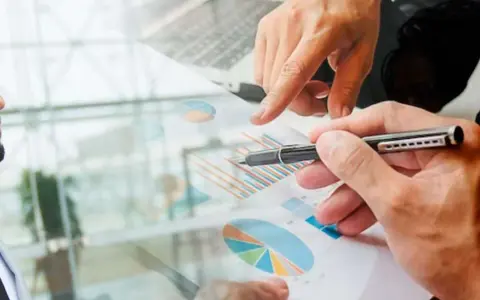 Un homme en costume regarde des graphiques financiers. Des mains analysent des données, suggérant une licence finance à distance.