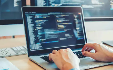 Des mains tapant sur un clavier d'ordinateur portable affichant du code. Une opportunité de formation informatique sans bac pour un avenir prometteur.